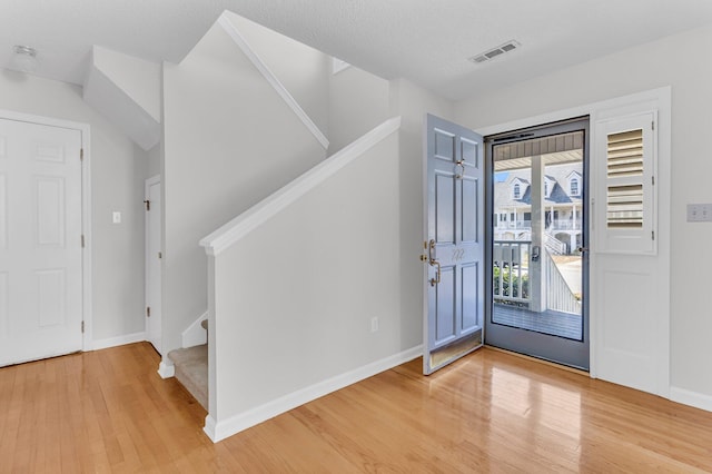 entryway featuring light wood-type flooring, baseboards, stairs, and visible vents