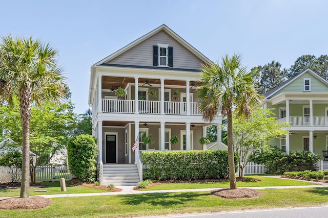 beach home featuring a front lawn, a balcony, ceiling fan, and covered porch