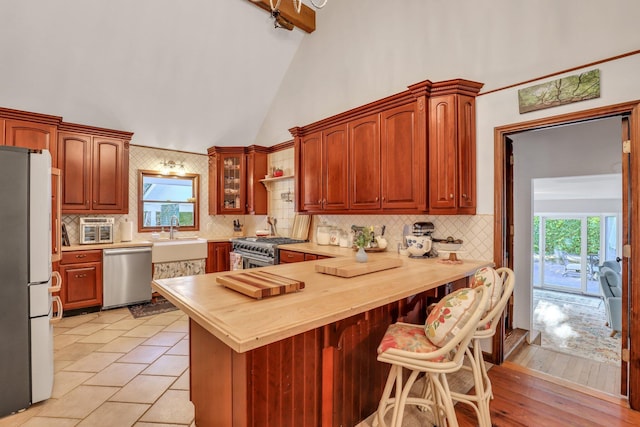 kitchen featuring backsplash, high vaulted ceiling, sink, butcher block counters, and stainless steel appliances