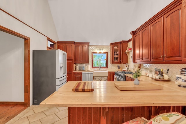 kitchen featuring a kitchen breakfast bar, high vaulted ceiling, kitchen peninsula, decorative backsplash, and appliances with stainless steel finishes