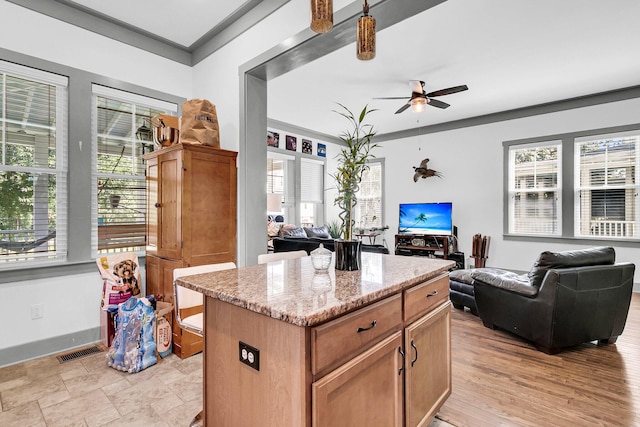 kitchen with a kitchen island, ceiling fan, light stone counters, and light hardwood / wood-style flooring