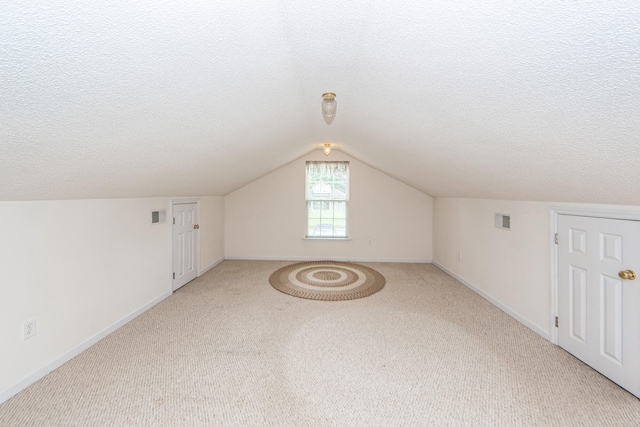 additional living space featuring a textured ceiling, lofted ceiling, and carpet flooring