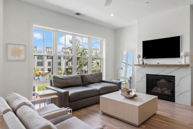 living area featuring recessed lighting, visible vents, light wood-style flooring, a premium fireplace, and a ceiling fan