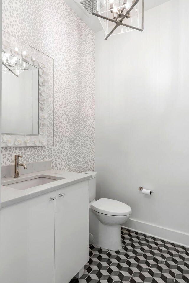 half bathroom with wallpapered walls, vanity, toilet, and baseboards