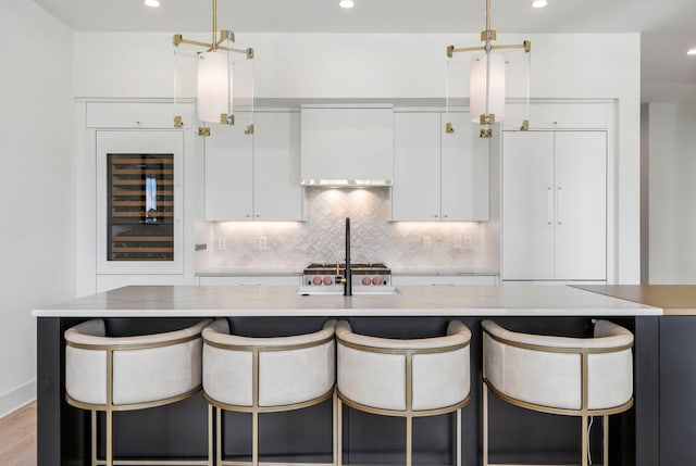 kitchen with beverage cooler, a kitchen bar, white cabinetry, and backsplash