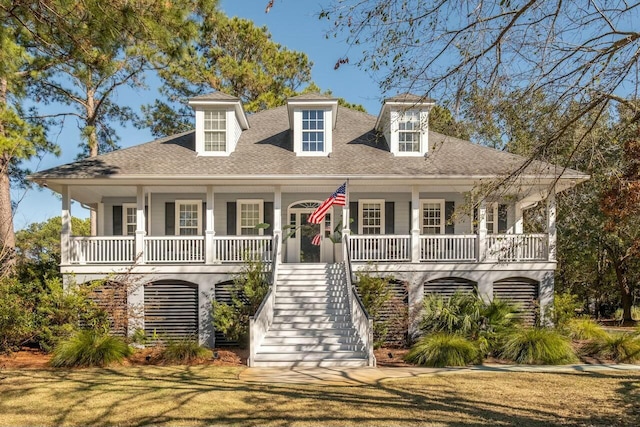 coastal home with a front yard, stairway, a porch, and roof with shingles