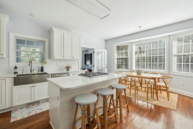 kitchen featuring stainless steel gas cooktop, a sink, white cabinetry, a center island, and pendant lighting