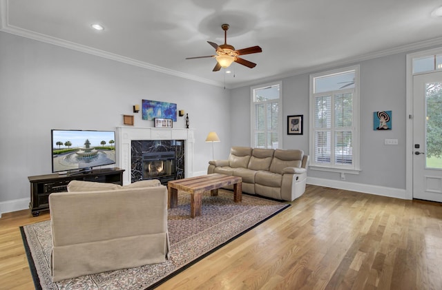 living room with baseboards, ornamental molding, ceiling fan, a fireplace, and light wood finished floors