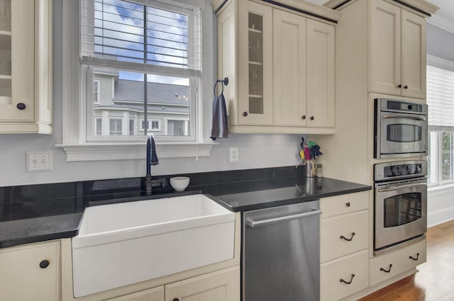 kitchen with a sink, glass insert cabinets, dark countertops, and dishwasher