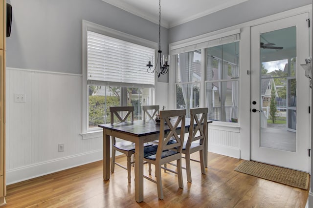 dining space featuring wainscoting, ceiling fan with notable chandelier, ornamental molding, and wood finished floors