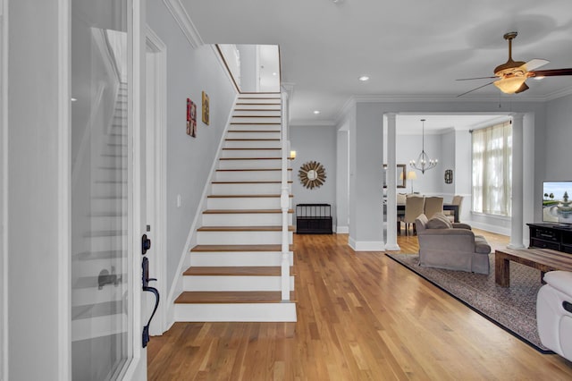 entrance foyer with crown molding, ceiling fan with notable chandelier, wood finished floors, and stairs