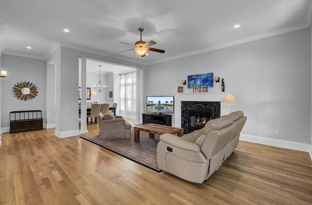 living area featuring baseboards, a high end fireplace, wood finished floors, and ceiling fan with notable chandelier