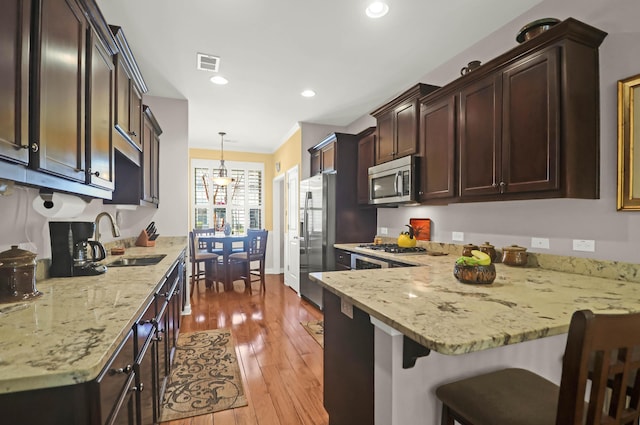 kitchen featuring visible vents, a peninsula, a sink, stainless steel appliances, and light wood-type flooring