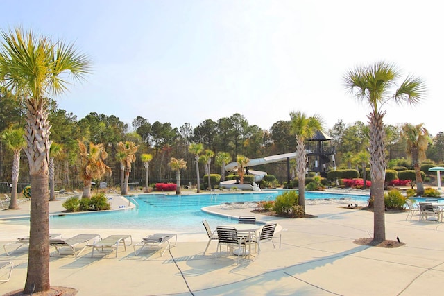 community pool with a patio area, a water slide, and fence