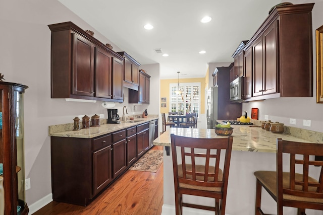 kitchen featuring light stone counters, a peninsula, wood finished floors, stainless steel appliances, and a sink