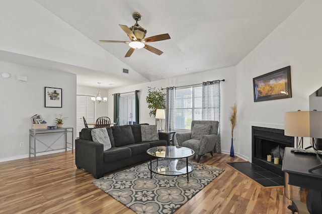 living area with ceiling fan with notable chandelier, a fireplace with flush hearth, wood finished floors, lofted ceiling, and visible vents