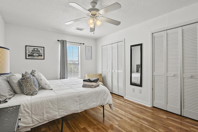 bedroom with visible vents, two closets, wood finished floors, baseboards, and a textured ceiling