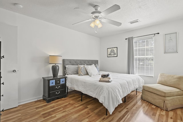 bedroom featuring a ceiling fan, a textured ceiling, visible vents, and wood finished floors