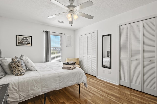 bedroom featuring visible vents, two closets, light wood-style floors, baseboards, and a textured ceiling
