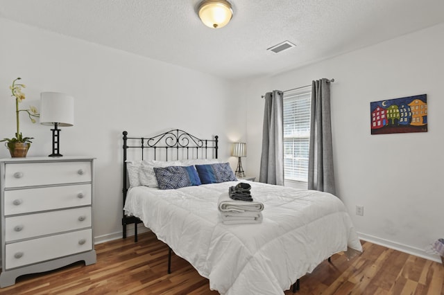 bedroom featuring a textured ceiling, baseboards, and wood finished floors