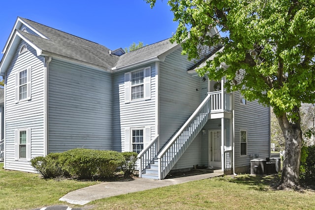 exterior space with stairway, roof with shingles, and a front lawn