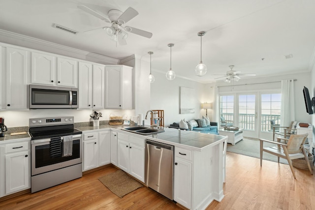 kitchen featuring a peninsula, a sink, visible vents, ornamental molding, and appliances with stainless steel finishes