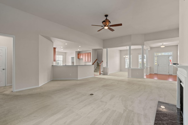 unfurnished living room with light colored carpet, ceiling fan with notable chandelier, and decorative columns