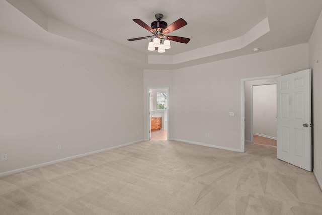 spare room featuring ceiling fan, light colored carpet, and a raised ceiling