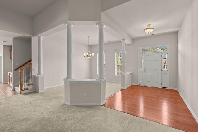 carpeted entryway featuring decorative columns and a notable chandelier