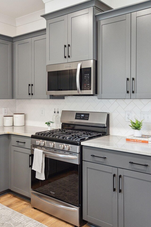 kitchen with appliances with stainless steel finishes, tasteful backsplash, light wood finished floors, and gray cabinets