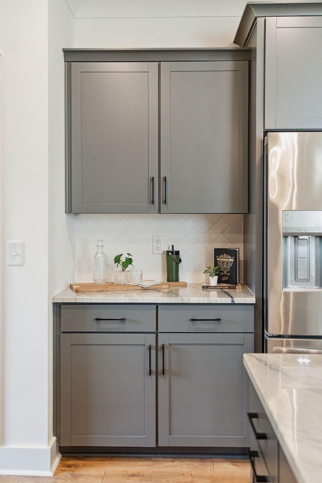 bar featuring decorative backsplash, light wood-style flooring, stainless steel fridge, and baseboards