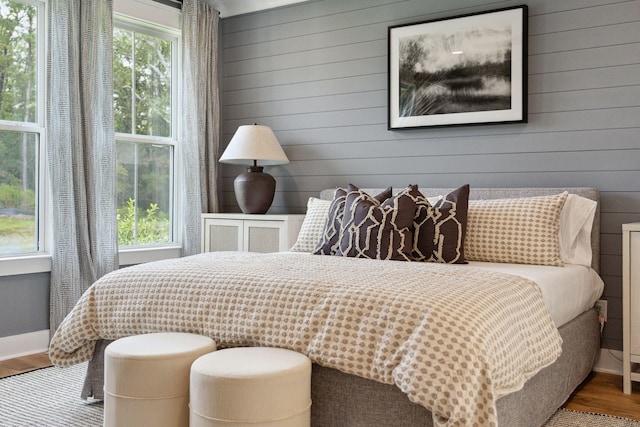 bedroom featuring baseboards, wood walls, wood finished floors, and multiple windows