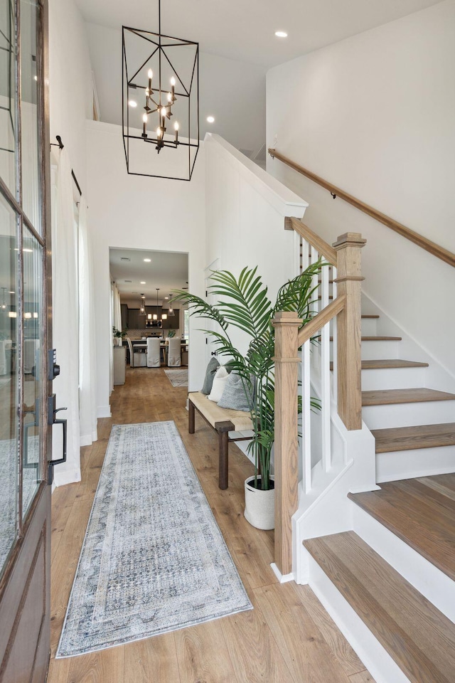foyer with recessed lighting, a high ceiling, stairway, a chandelier, and wood finished floors