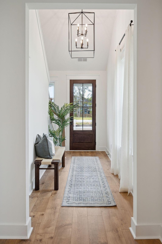 doorway to outside featuring light wood finished floors, visible vents, a notable chandelier, and baseboards