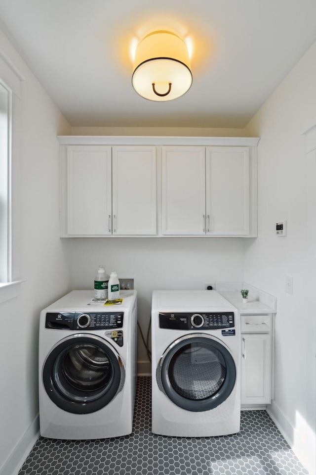 clothes washing area featuring washing machine and clothes dryer, cabinet space, and baseboards