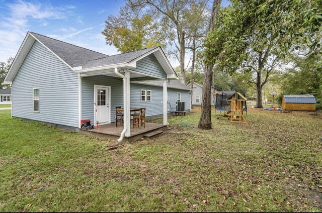 rear view of house featuring a playground, a deck, a storage unit, a lawn, and central AC