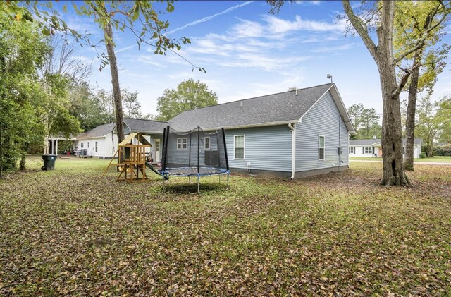 rear view of house with a playground, a trampoline, and a lawn