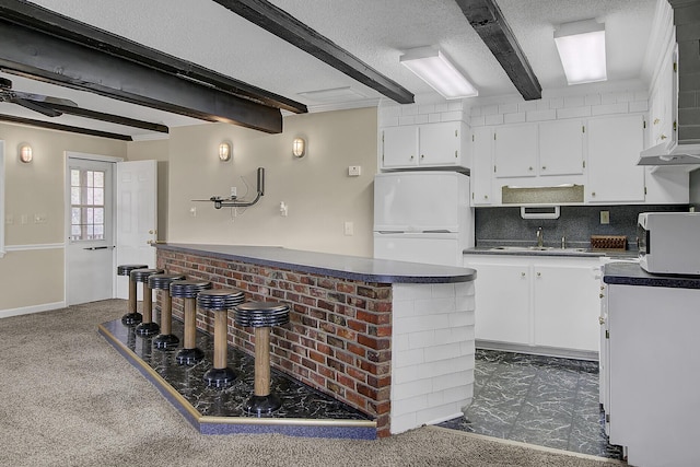 kitchen with white cabinetry, beamed ceiling, and dark colored carpet