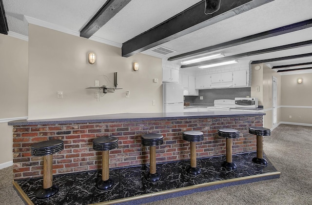 kitchen with white appliances, white cabinets, dark colored carpet, beamed ceiling, and kitchen peninsula