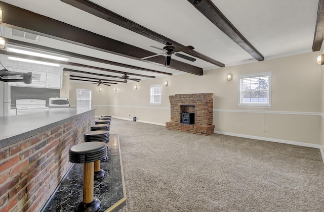 living room featuring carpet, ceiling fan, a fireplace, beamed ceiling, and brick wall