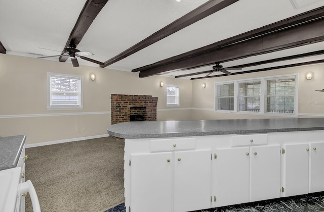 kitchen with dark colored carpet, beam ceiling, white cabinetry, and a brick fireplace