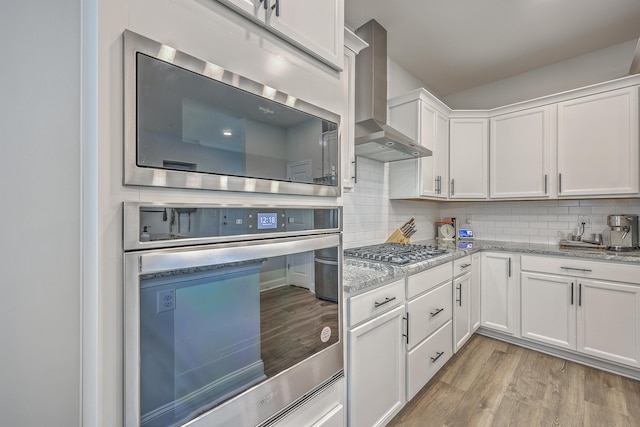 kitchen featuring light wood finished floors, wall chimney exhaust hood, tasteful backsplash, and appliances with stainless steel finishes