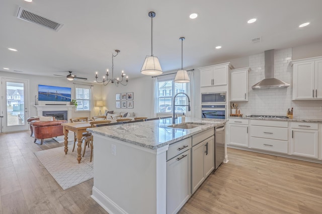 kitchen featuring visible vents, a sink, appliances with stainless steel finishes, wall chimney exhaust hood, and light wood finished floors