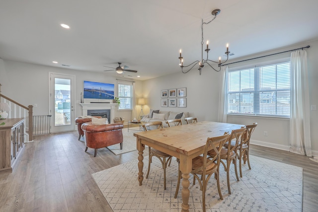 dining space with wood finished floors, baseboards, recessed lighting, a glass covered fireplace, and ceiling fan with notable chandelier