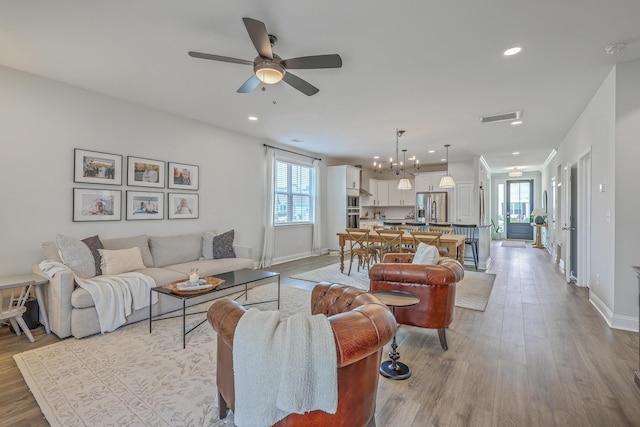 living room with visible vents, ceiling fan with notable chandelier, baseboards, and wood finished floors