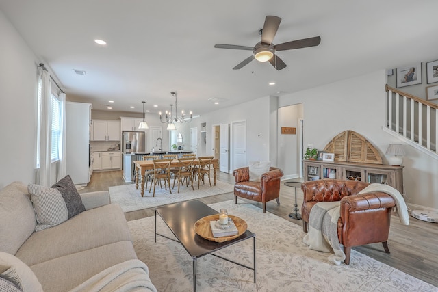 living area featuring recessed lighting, ceiling fan with notable chandelier, visible vents, and light wood finished floors