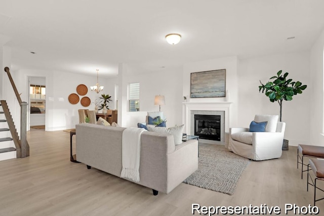 living room featuring a notable chandelier, stairway, light wood-style flooring, and a fireplace with flush hearth