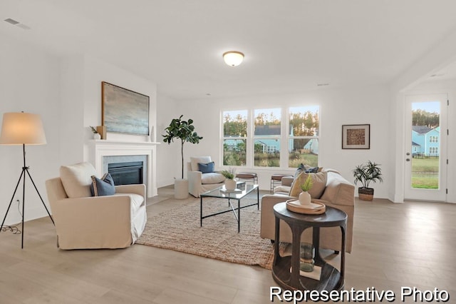 living room featuring a fireplace with flush hearth, light wood-style floors, and visible vents