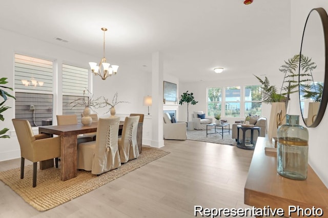 dining area with light wood-style flooring, a fireplace, visible vents, and a chandelier