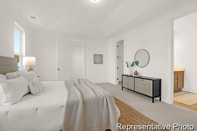 carpeted bedroom featuring a tray ceiling, baseboards, visible vents, and ensuite bathroom